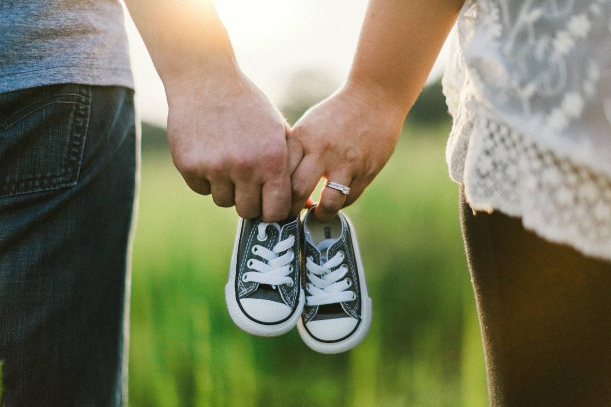 Expecting parents holding hands while carrying tiny baby shoes