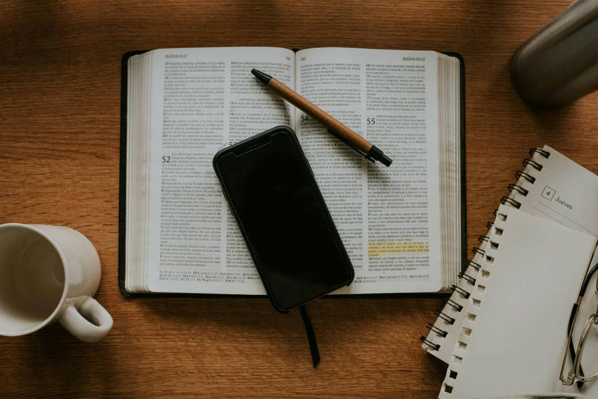Open Bible with a pen and phone resting on the page, notebook nearby